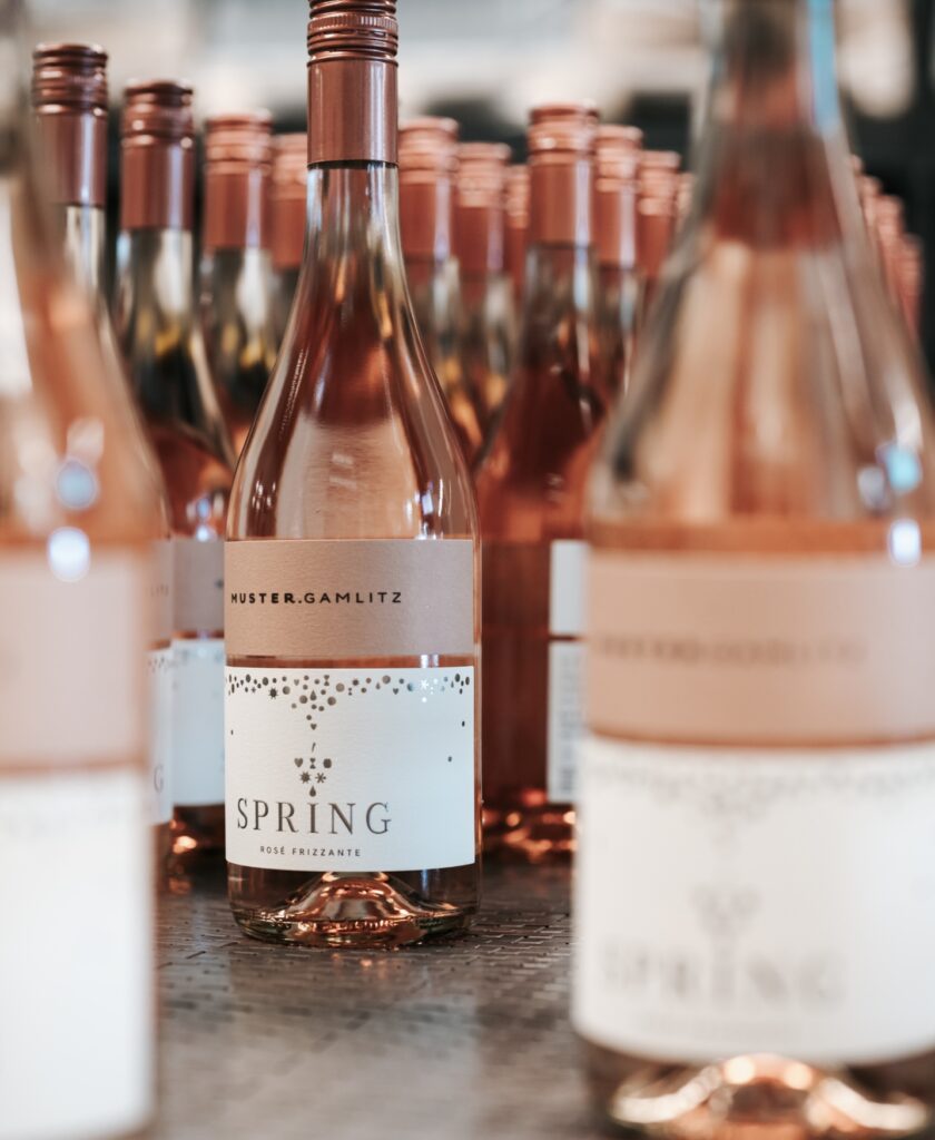 Mehrere Flaschen Roséwein mit Etikett 'MUSTER.GAMLITZ Spring Rosé Frizzante' in einer Reihe