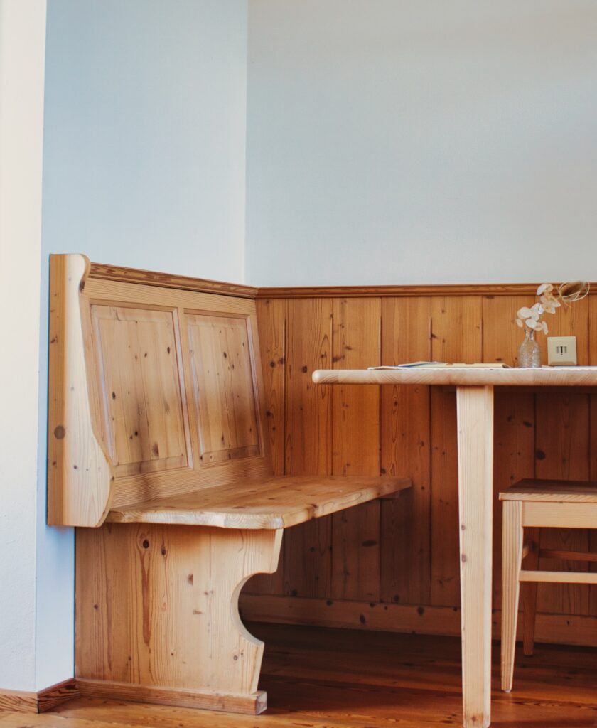 Holzeckbank mit Rückenlehne an einer holzvertäfelten Wand neben einem Holztisch und einem Stuhl