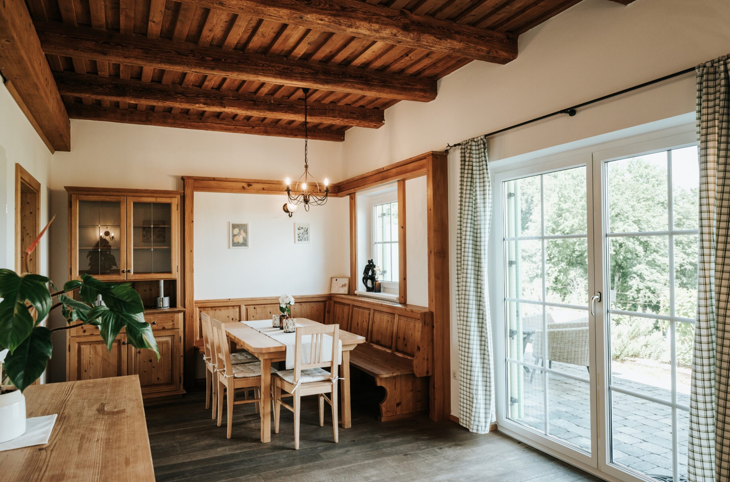 Esszimmer mit Holztisch, Eckbank, Stühlen, Holzdecke mit Balken und großen Fenstern mit Blick auf Terrasse